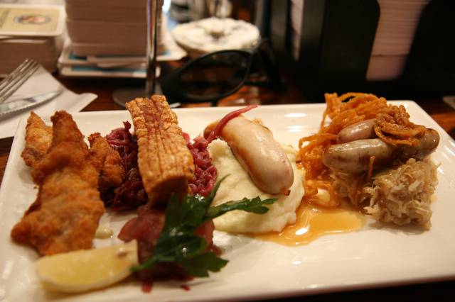 Hearty Bavarian food on a fancy plate. Left to right: Schnitzel, pork belly (Schweinebauch) with red cabbage (Rotkohl), Weißwurst with mashed potatoes (Kartoffelpüree), Bratwurst on sauerkraut