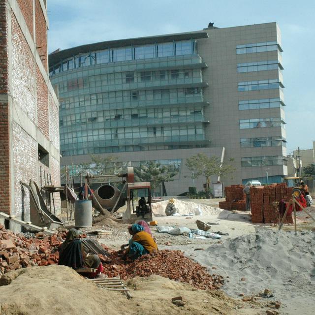 Where modern India meets ancient Bharat: workers crushing bricks by hand in front of a 21st century office building