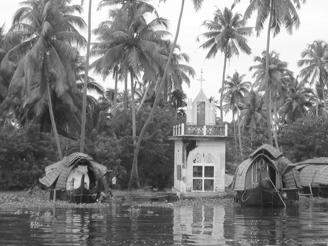 A small christian chapel along a backwater canal, with traditional houseboats moored beside it.