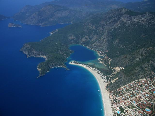 Blue Lagoon in the centre with the surrounding coves and mountains. In the lower right of the photo is the town of Ölüdeniz.