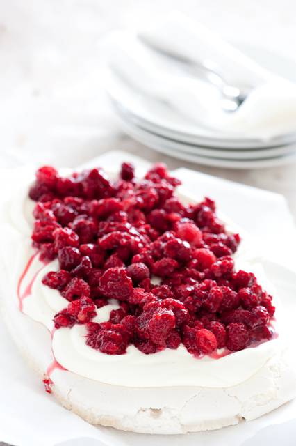 A pavlova garnished with cream and raspberries