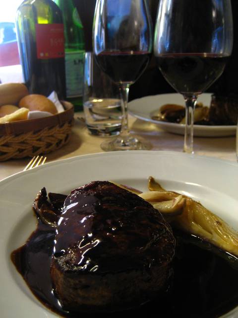 A traditional Italian meal, with beef with sauce and dark red wine.