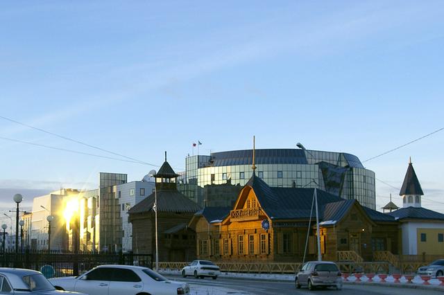 Russian-Asian bank (from the end 19th century). To the left is a tower of the Yakutsk ostrog (palisade tower), the city symbol. Behind is the glass façade of the Komdragmeta building.