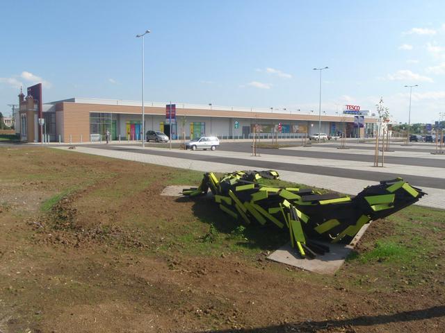 Tesco Kőszeg with Statue of living here Fire Salamander. On the left side of the building a wall sections what remained the former baize factory. At background is a history museum about the local textile industry.