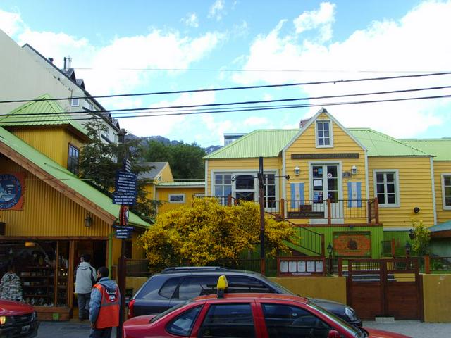 Traditional Patagonian house at the shopping street San Martín. Left of it there's a sign showing distances to major cities in the world